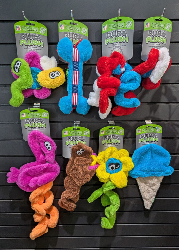 Bright plush dog toys spelling 'DURA PLUSH' in various colors on a retail display wall.